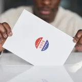 A voter placing a ballot into a box during an election. Focus on the act of voting.