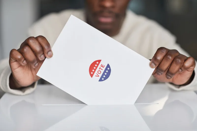 A voter placing a ballot into a box during an election. Focus on the act of voting.