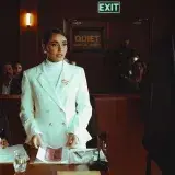 A lawyer in white suit confidently presents a case during a courtroom session with colleagues and audience.