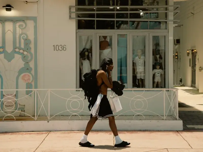 Man walking past a Miami boutique carrying shopping bags in the summer sun.