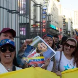 A vibrant street protest in Venezuela, showcasing joyous participants holding a political figure's portrait amid flags and smiles.
