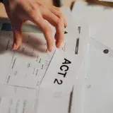 A person's hand organizing screenplay documents with focus on 'ACT 2' in an office setting.