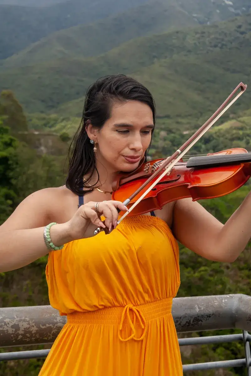 Woman in yellow dress playing violin with mountainous backdrop in Mérida, Venezuela.
