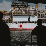 Silhouetted figures observing a large offshore oil rig at sea, emphasizing maritime industry.