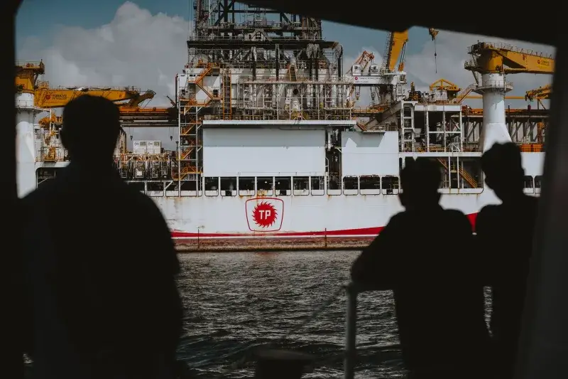 Silhouetted figures observing a large offshore oil rig at sea, emphasizing maritime industry.