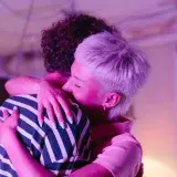 Two adults hugging warmly in a neon-lit room, creating a cozy, intimate atmosphere.