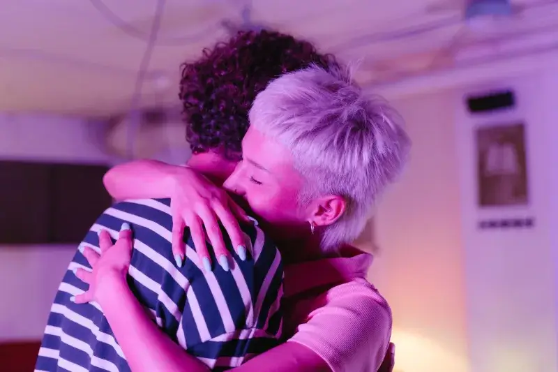 Two adults hugging warmly in a neon-lit room, creating a cozy, intimate atmosphere.