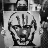 Black and white image of a protester holding a portrait of Putin marked with a handprint.