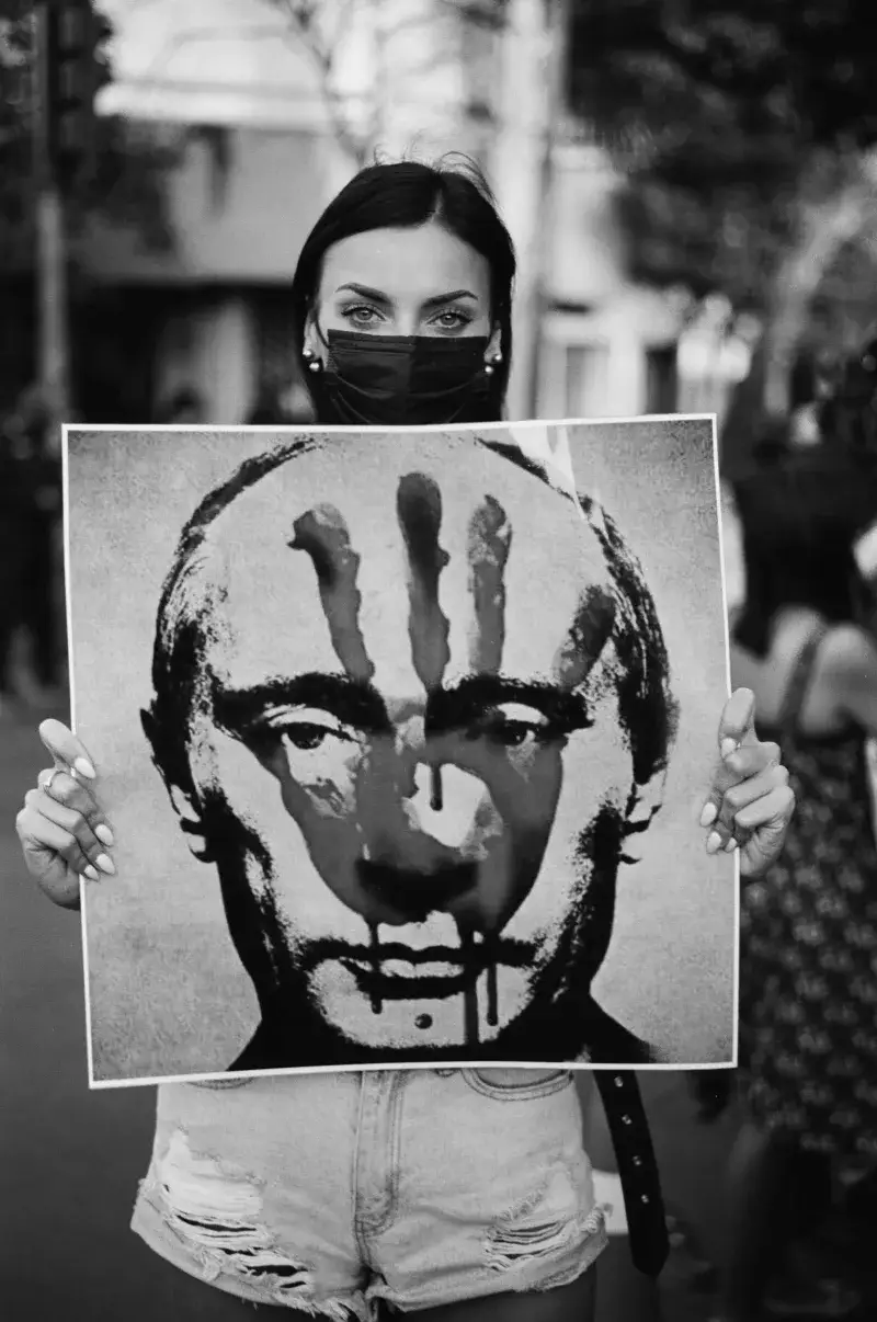 Black and white image of a protester holding a portrait of Putin marked with a handprint.