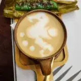 A beautifully crafted latte art with a side of traditional Filipino dessert suman on a wooden tray.