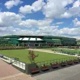 Exterior view of the Wimbledon tennis venue with a grassy area on a clear day, capturing its iconic architecture.