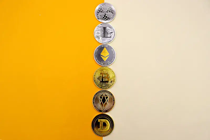A row of cryptocurrency coins including Bitcoin, Ethereum, and Dogecoin on a vibrant yellow surface.