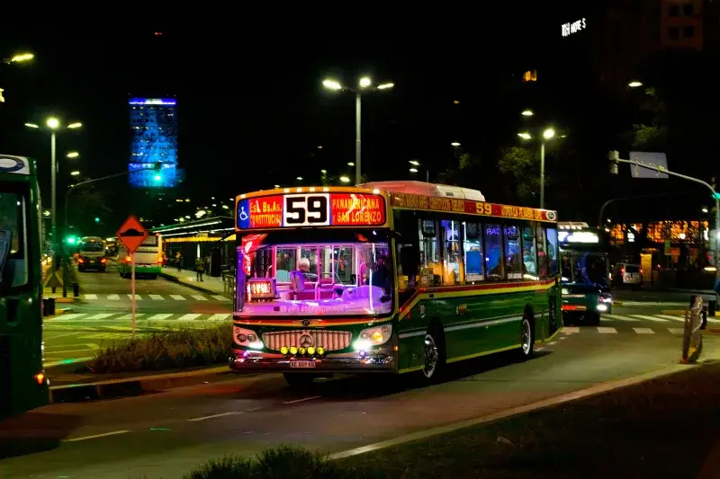 Brightly lit bus on Buenos Aires city street at night, showcasing urban transport.
