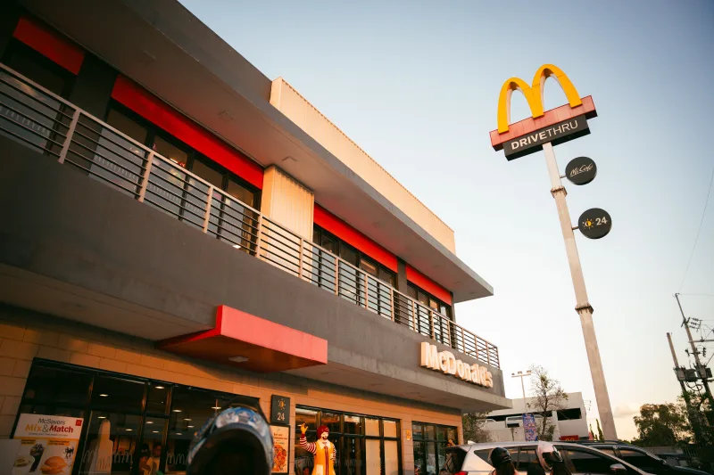 A modern McDonald's fast food restaurant with distinctive branding and drive-thru facilities under a clear blue sky.