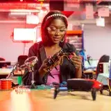 Black female engineer at desk assembling drones, showcasing electronics and technology in a modern lab setting.