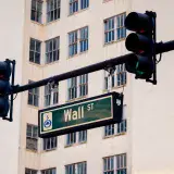 Traffic lights and Wall St sign in cityscape, symbolizing finance hub.