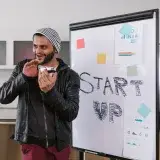 Hombre con chaqueta de cuero presenta entusiasmado una idea de startup en un pizarrón en el interior.