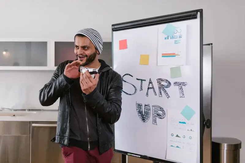 Hombre con chaqueta de cuero presenta entusiasmado una idea de startup en un pizarrón en el interior.