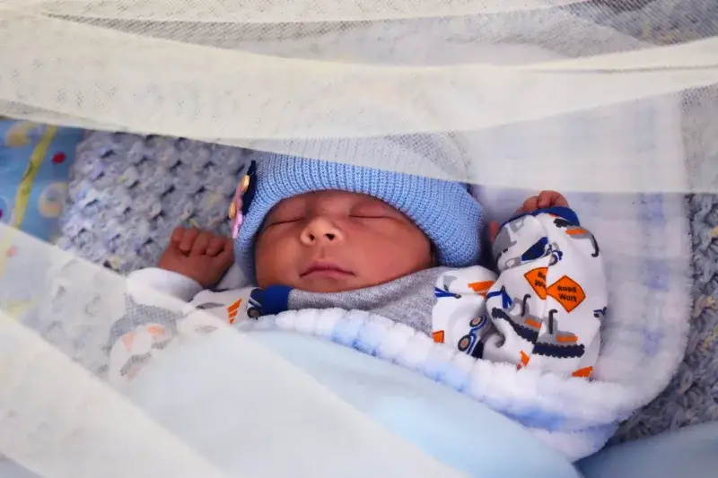 Close-up of a peacefully sleeping newborn baby in a cozy crib, wrapped in a soft blanket.