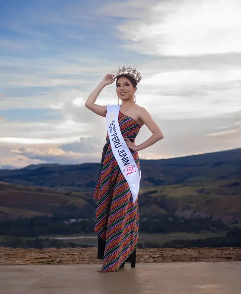 Elegant Miss Junín in a traditional dress and crown, set against a scenic sunset in Junín, Peru.