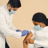 Close-up of a healthcare worker giving a vaccine injection to a woman wearing a face mask.
