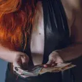 Close-up of woman with red hair in a leather outfit holding Argentine pesos.