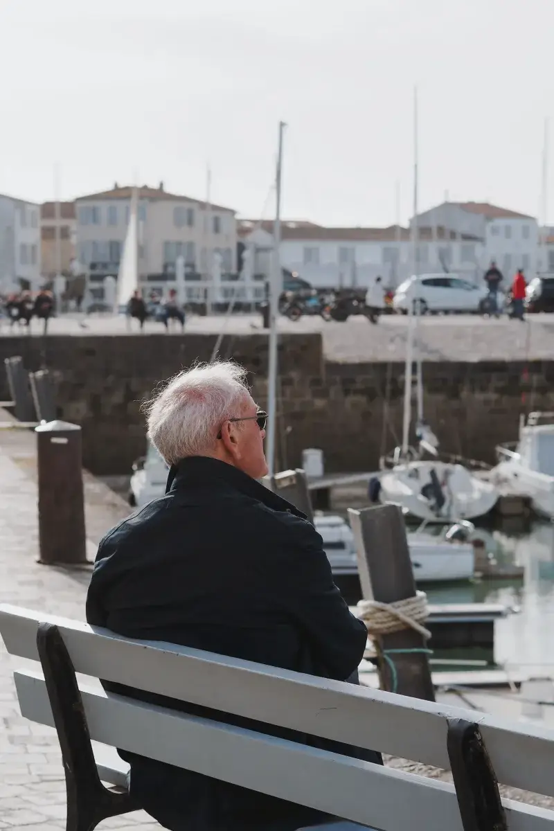 An elderly man sits peacefully overlooking a harbor in Nuova Aquitania, Francia, on a calm day.
