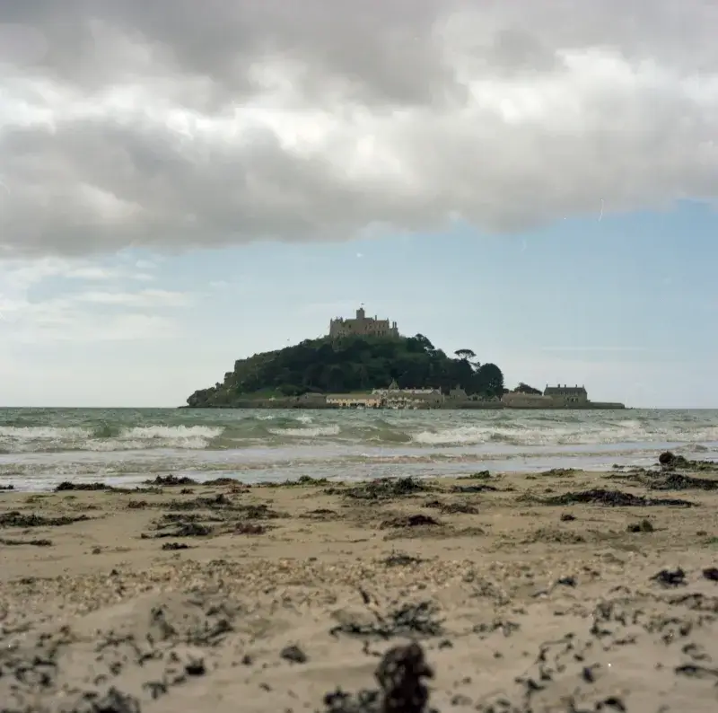 A view of Saint Michael's Mount from the beach under dramatic clouds.