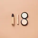 Flatlay of foundation, concealer, and compact powder on beige background. Perfect for beauty and cosmetic themes.
