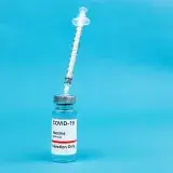 Vaccine and syringe on a blue backdrop, representing COVID-19 immunization and prevention.