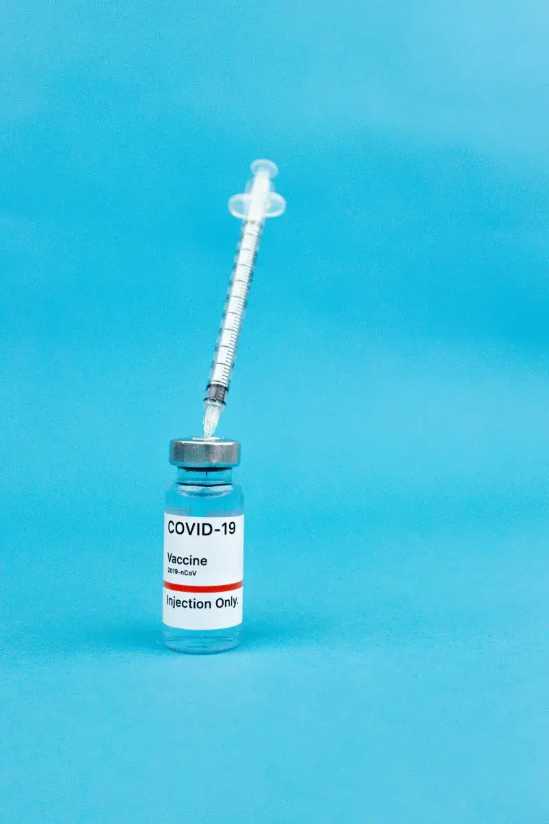 Vaccine and syringe on a blue backdrop, representing COVID-19 immunization and prevention.
