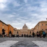 Crowds walking towards St. Peter's Basilica in the Vatican on a cloudy day.