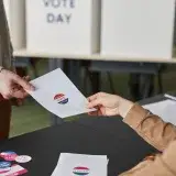 Two people exchanging a ballot paper during an indoor voting process.