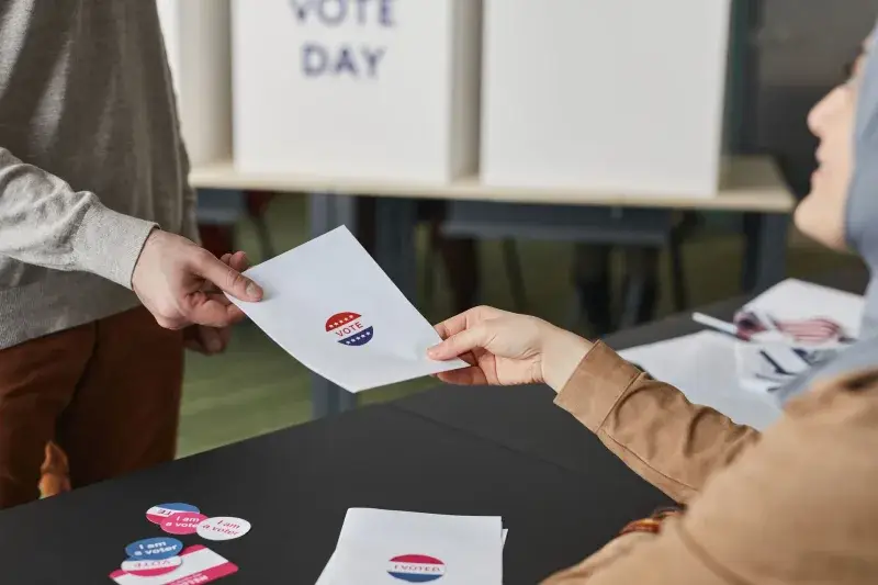 Two people exchanging a ballot paper during an indoor voting process.