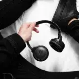 Person in black fashion holding JBL wireless headphones, showcasing modern tech vibe.