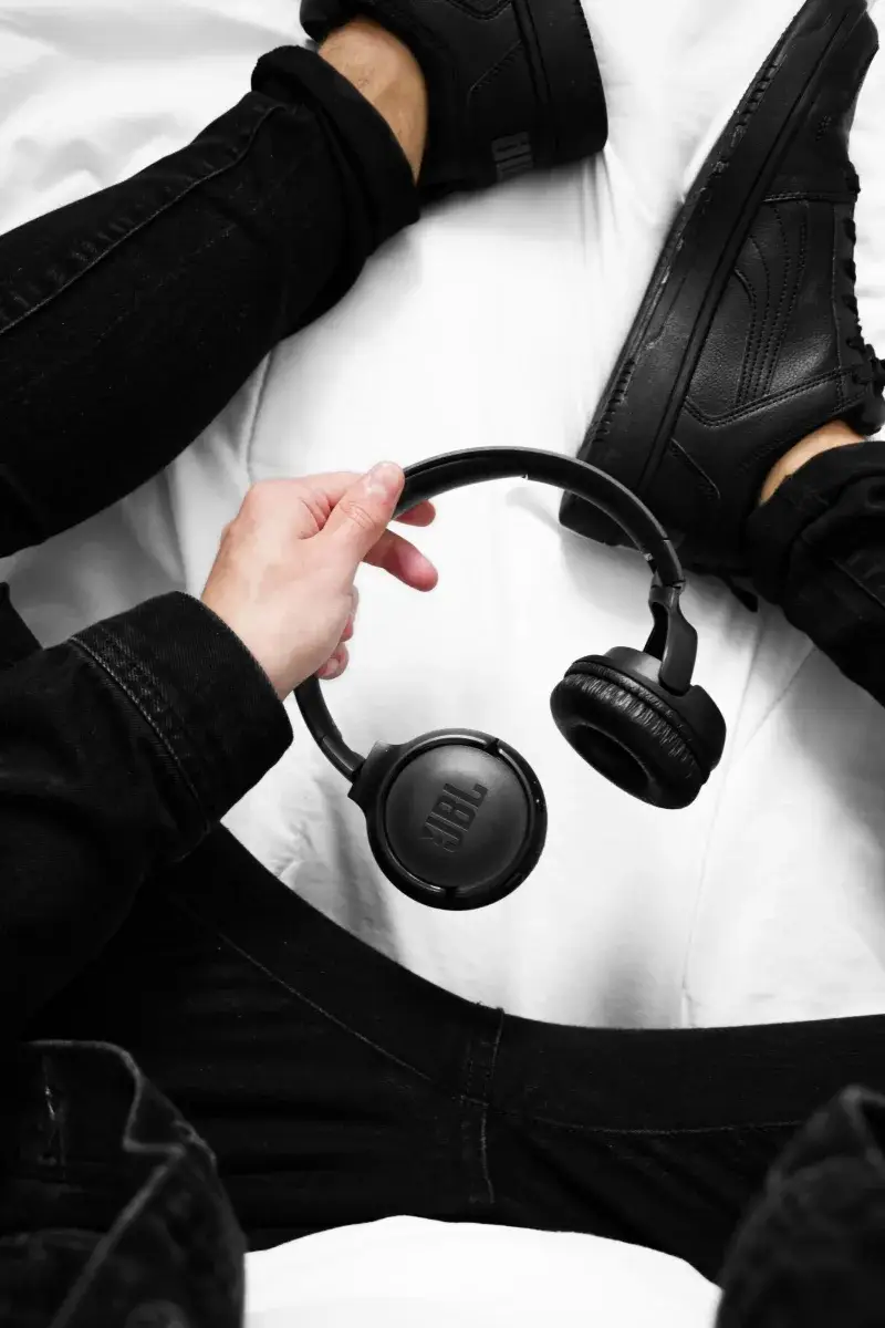Person in black fashion holding JBL wireless headphones, showcasing modern tech vibe.