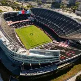 Aerial shot of a modern, empty soccer stadium surrounded by city buildings on a clear day.