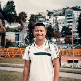 A cheerful man standing outdoors in Villamaría, Colombia, with a scenic backdrop of colorful buildings.