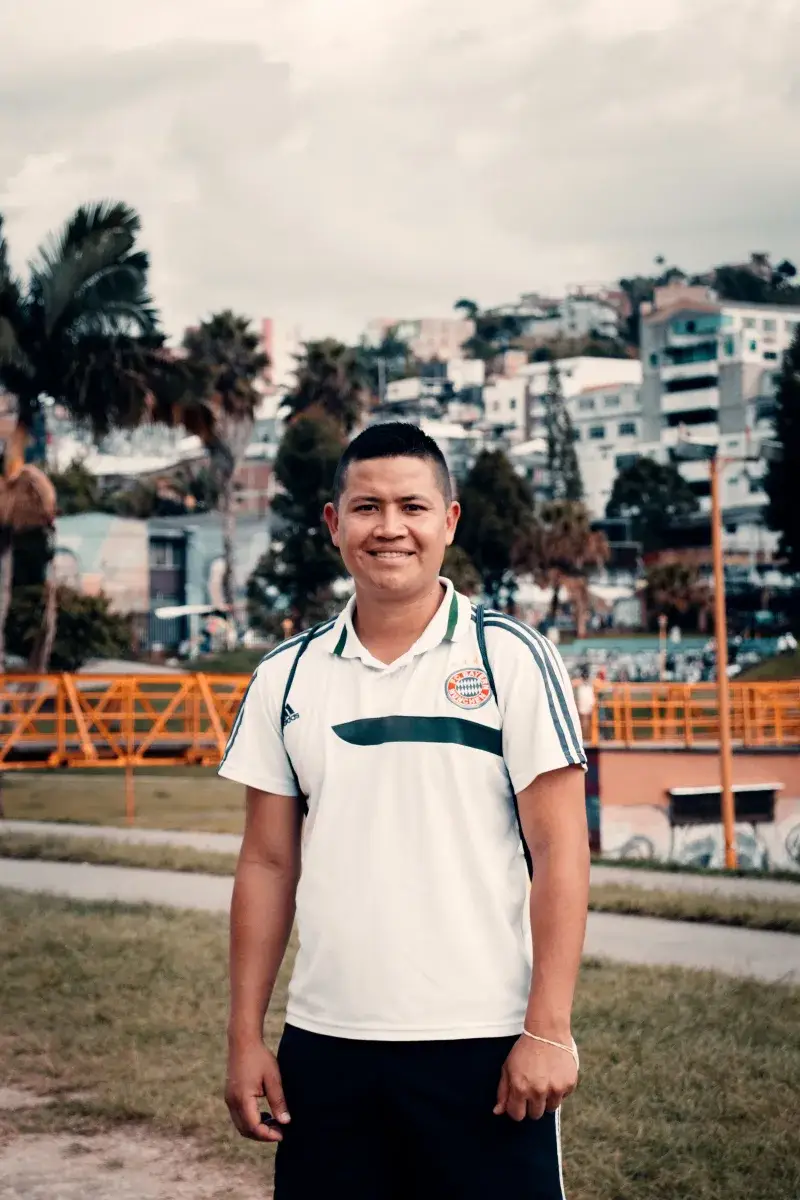 A cheerful man standing outdoors in Villamaría, Colombia, with a scenic backdrop of colorful buildings.