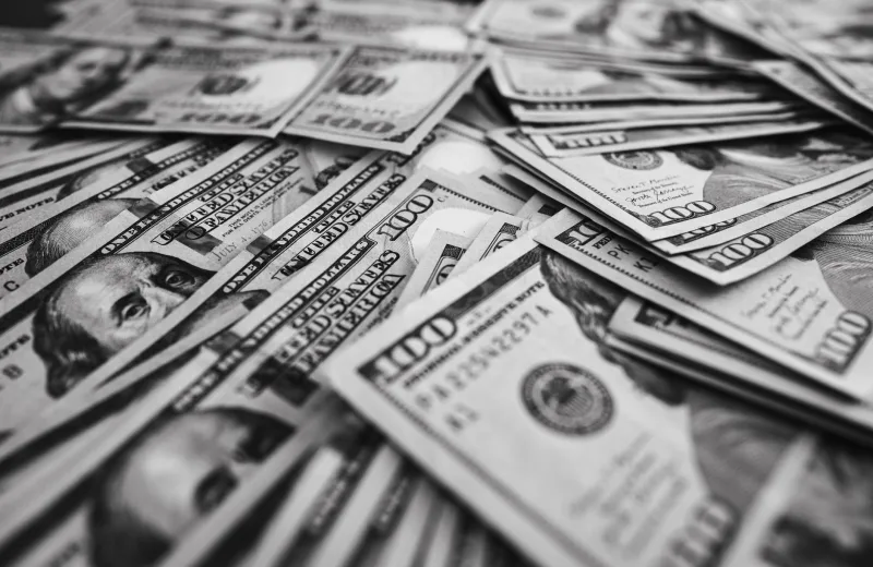 Monochrome image of scattered US hundred dollar bills representing wealth and prosperity.