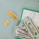 Close-up of U.S. dollars and Bitcoin coins placed on a weekly budget planner, symbolizing modern finance.