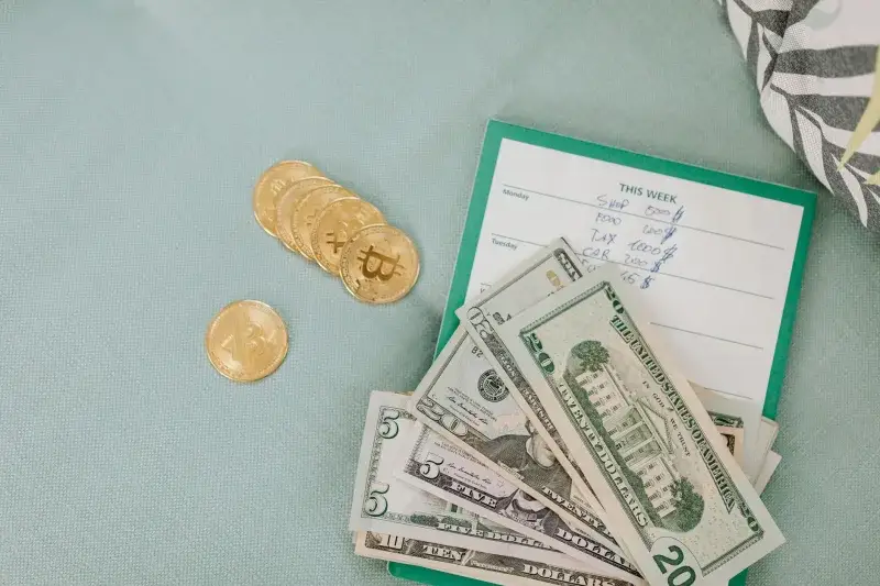 Close-up of U.S. dollars and Bitcoin coins placed on a weekly budget planner, symbolizing modern finance.