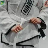 Close-up image of a martial artist tying their judo gi belt, showcasing Brazilian and Keiko logos.