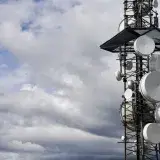 A telecommunication tower equipped with satellite dishes against a cloudy sky.