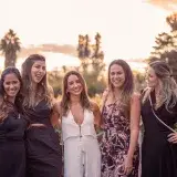 A group of five stylish women posing outdoors at sunset, exuding elegance and friendship.