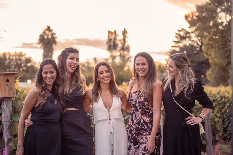 A group of five stylish women posing outdoors at sunset, exuding elegance and friendship.