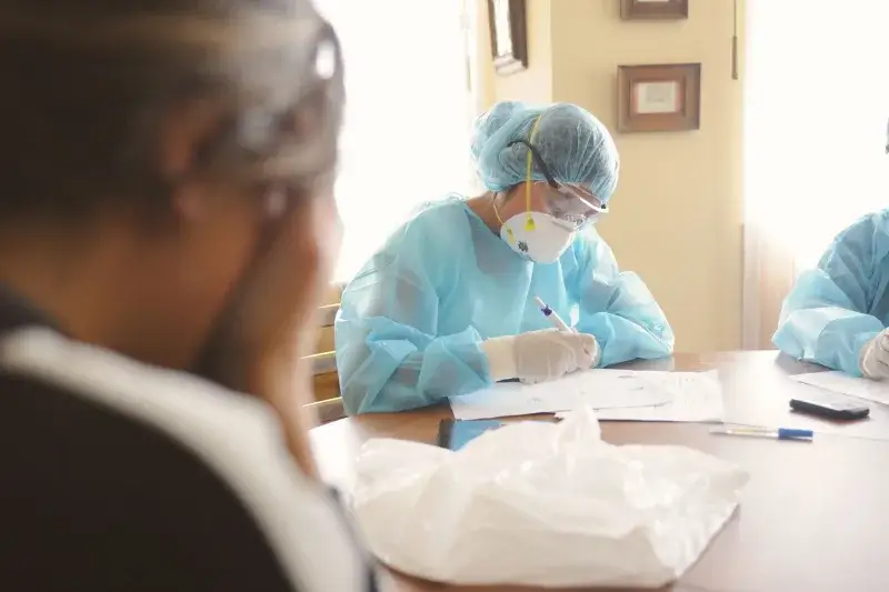 Medical professionals in PPE working at a desk during a daytime setting indoors.