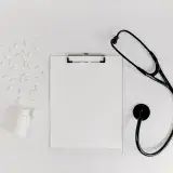 Flat lay of clipboard, pills, and stethoscope for medical use.