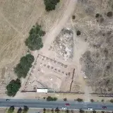 Aerial shot of a rural construction site with surrounding landscape and vehicles on a road.