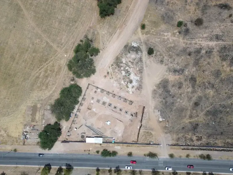 Aerial shot of a rural construction site with surrounding landscape and vehicles on a road.